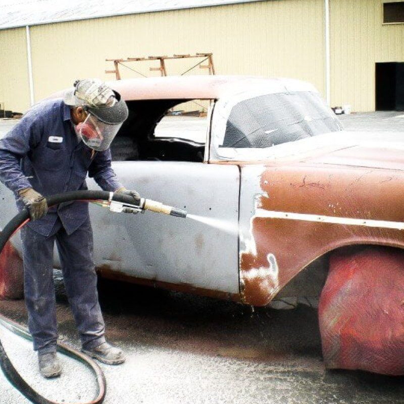 A worker sandblasts an old car's rusty door.